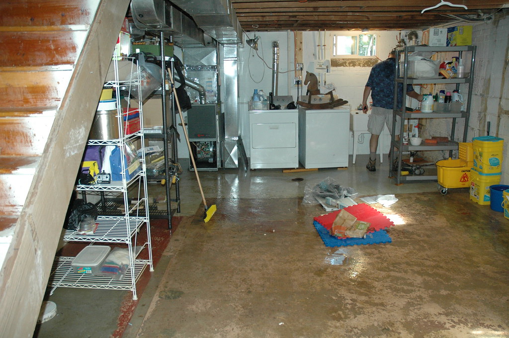 Homeowner cleaning up standing water and damaged belongings in a partially flooded suburban basement